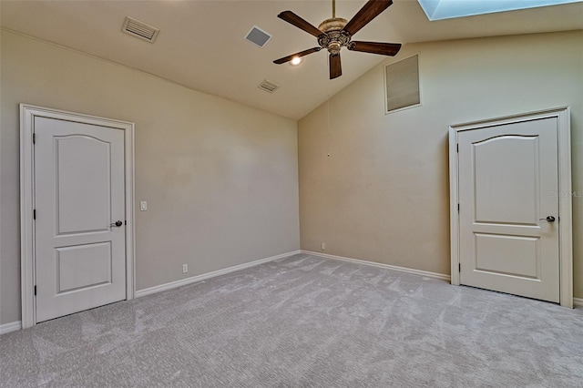 carpeted spare room featuring a skylight, high vaulted ceiling, and ceiling fan