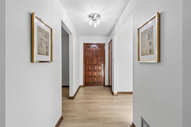 hall with a textured ceiling and light hardwood / wood-style flooring