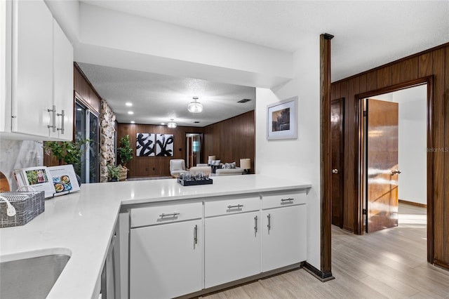 kitchen featuring white cabinetry, wooden walls, a textured ceiling, and light hardwood / wood-style floors