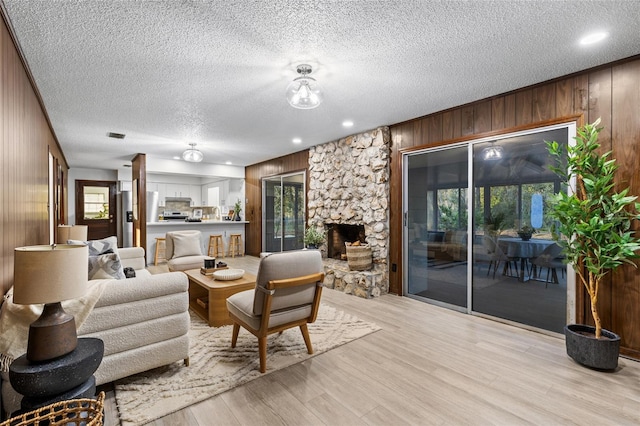 living room with light hardwood / wood-style flooring, a stone fireplace, wooden walls, and a textured ceiling