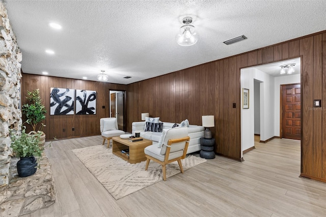 living room featuring wooden walls, light hardwood / wood-style floors, and a textured ceiling