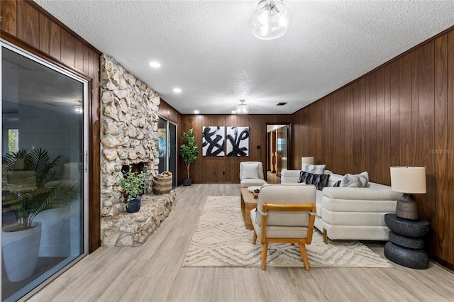 living room with a fireplace, wood walls, a textured ceiling, and light hardwood / wood-style flooring