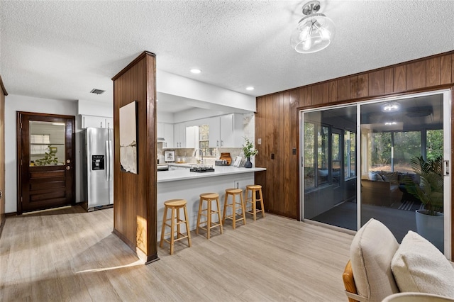 kitchen featuring wood walls, white cabinetry, stainless steel fridge, kitchen peninsula, and light wood-type flooring