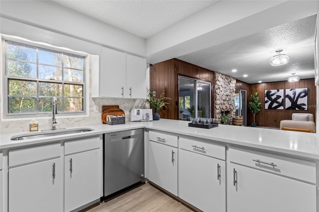 kitchen featuring wooden walls, white cabinetry, sink, stainless steel dishwasher, and a textured ceiling