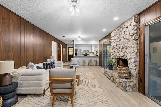 living room with light hardwood / wood-style flooring, a textured ceiling, a fireplace, and wood walls