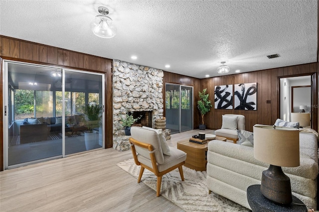 living room with wooden walls, a fireplace, light hardwood / wood-style flooring, and a textured ceiling