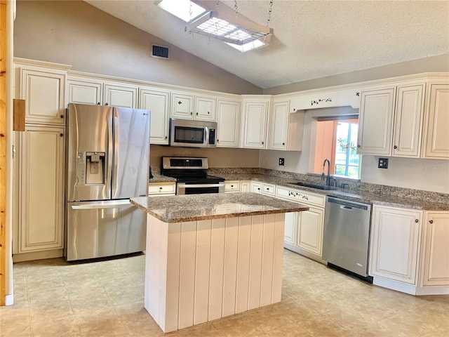 kitchen featuring lofted ceiling, sink, stainless steel appliances, a center island, and stone countertops