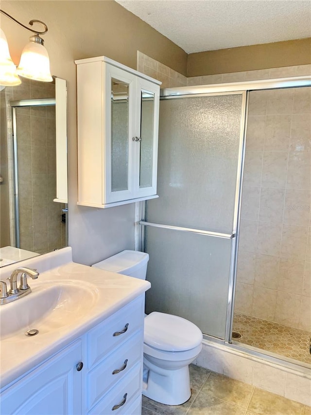 bathroom featuring tile patterned floors, toilet, a textured ceiling, vanity, and a shower with door