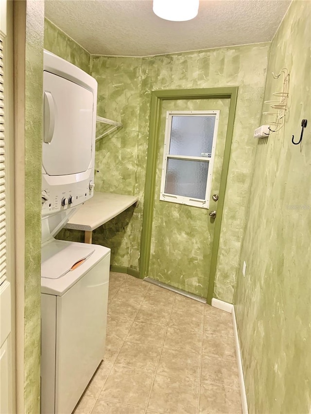 laundry area featuring light tile patterned floors, stacked washer and clothes dryer, and a textured ceiling