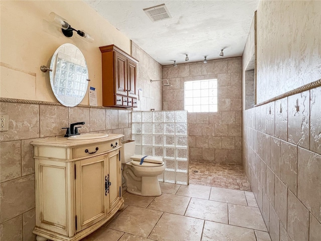 bathroom featuring tiled shower, tile walls, a textured ceiling, and toilet