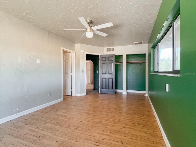 unfurnished bedroom featuring multiple closets, ceiling fan, a textured ceiling, and light wood-type flooring