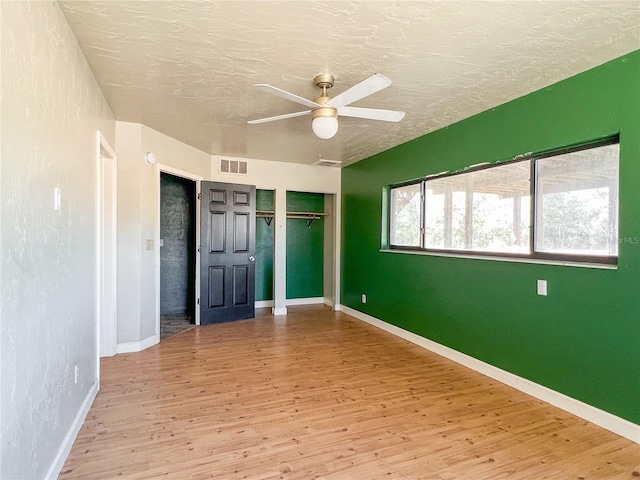 unfurnished bedroom with hardwood / wood-style floors, two closets, a textured ceiling, and ceiling fan