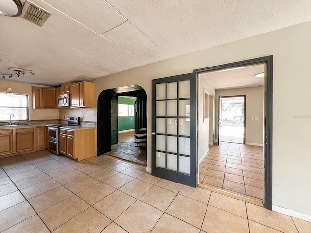 kitchen with sink, light tile patterned floors, stainless steel appliances, and a textured ceiling