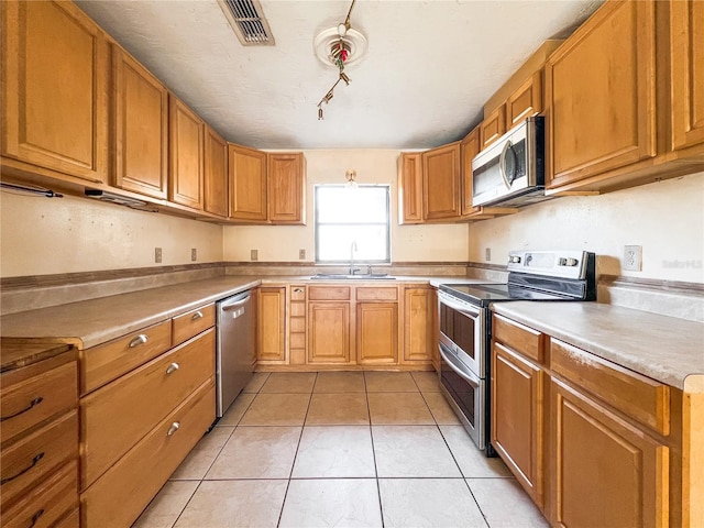 kitchen featuring sink, light tile patterned floors, track lighting, and stainless steel appliances