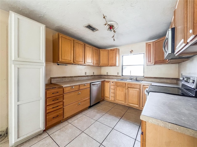 kitchen with sink, light tile patterned floors, a textured ceiling, and appliances with stainless steel finishes