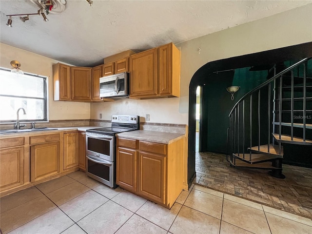 kitchen with appliances with stainless steel finishes, sink, a textured ceiling, and light tile patterned floors