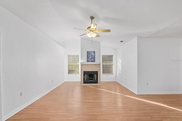 unfurnished living room with light wood finished floors, lofted ceiling, a tiled fireplace, a ceiling fan, and baseboards