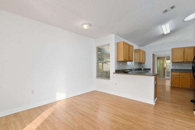 kitchen with light wood-type flooring, dark countertops, visible vents, and decorative backsplash