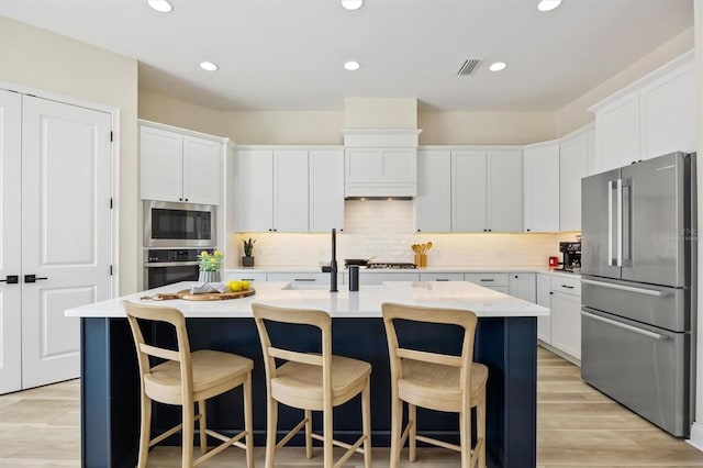 kitchen featuring light countertops, appliances with stainless steel finishes, an island with sink, and visible vents