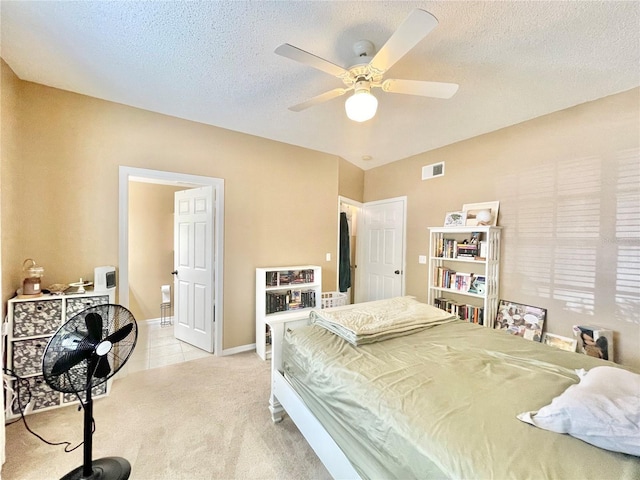 bedroom with ceiling fan, ensuite bath, light carpet, and a textured ceiling