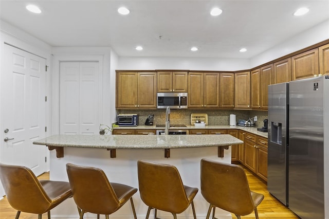 kitchen with a kitchen breakfast bar, stainless steel appliances, light stone countertops, a center island with sink, and light hardwood / wood-style flooring