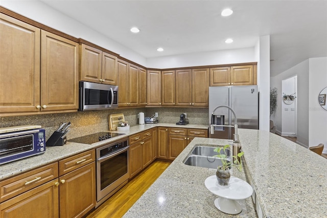 kitchen with sink, stainless steel appliances, tasteful backsplash, light hardwood / wood-style floors, and light stone countertops