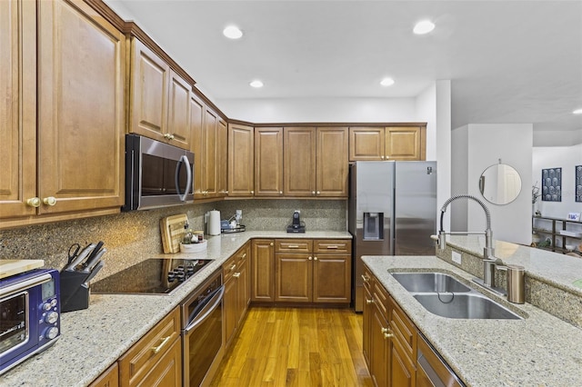 kitchen featuring light stone countertops, appliances with stainless steel finishes, sink, and light hardwood / wood-style flooring