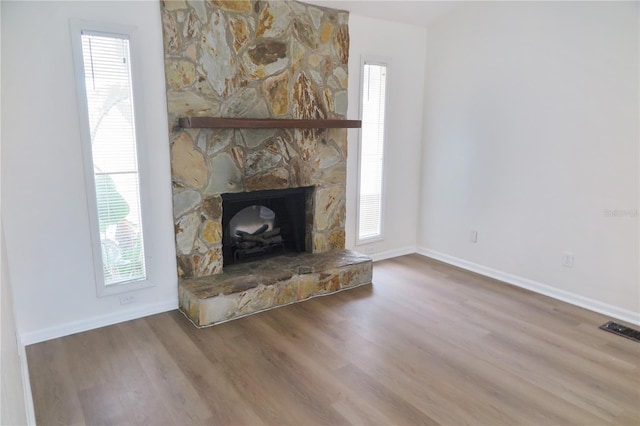 unfurnished living room featuring hardwood / wood-style flooring, a stone fireplace, and a healthy amount of sunlight