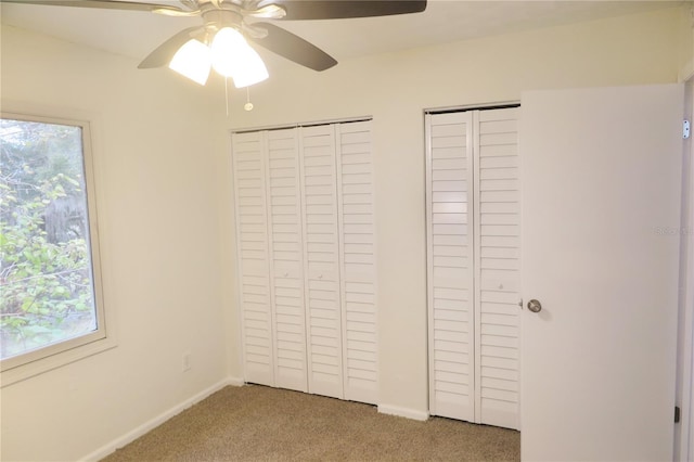 unfurnished bedroom featuring multiple windows, carpet flooring, two closets, and ceiling fan