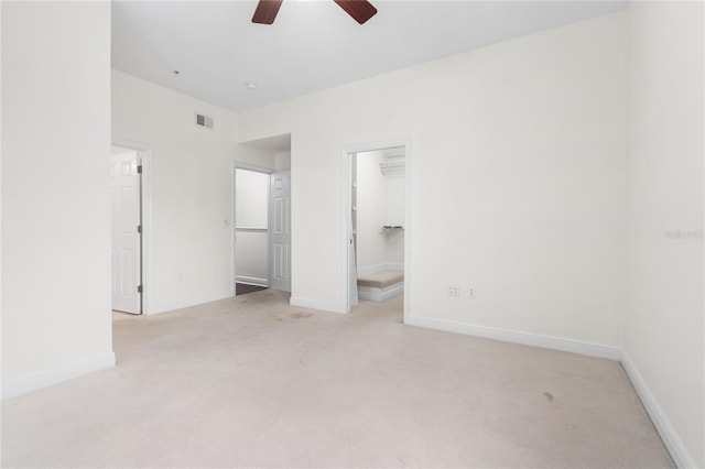 unfurnished bedroom featuring light carpet, a spacious closet, a closet, and ceiling fan