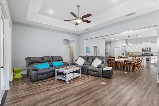 living room featuring a tray ceiling, wood-type flooring, and ceiling fan with notable chandelier