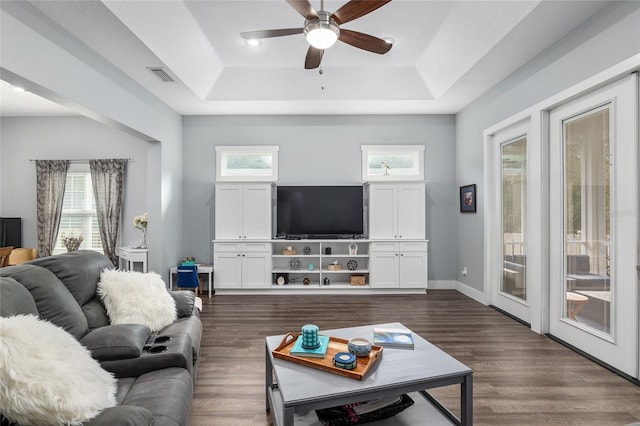 living room with a tray ceiling, dark wood-type flooring, and a wealth of natural light