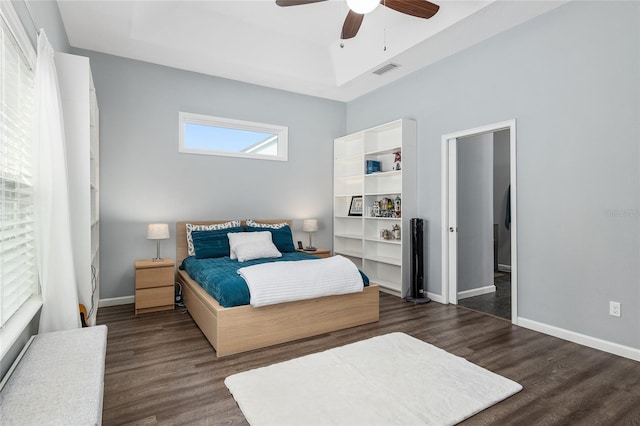 bedroom with dark wood-type flooring, ceiling fan, and a tray ceiling