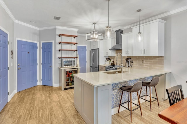 kitchen with visible vents, freestanding refrigerator, light countertops, wall chimney range hood, and a sink