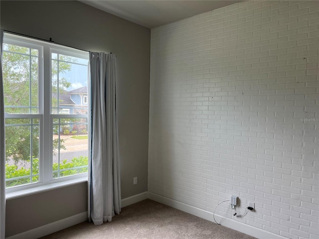 unfurnished room with carpet, baseboards, and brick wall