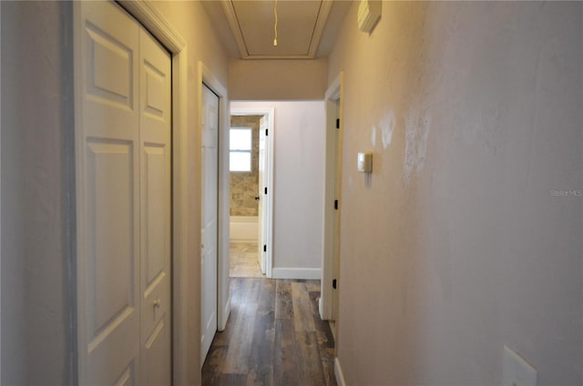 hallway featuring attic access, dark wood-style flooring, and baseboards