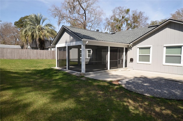 rear view of house featuring roof with shingles, a yard, a sunroom, a patio area, and fence