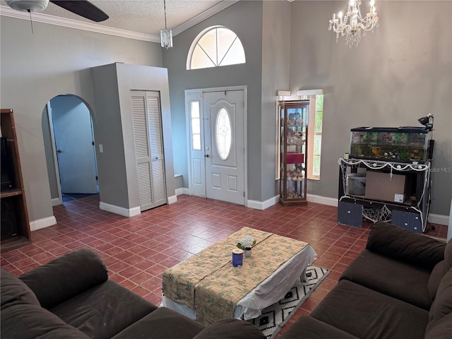 tiled living room with crown molding, ceiling fan with notable chandelier, a textured ceiling, and a high ceiling