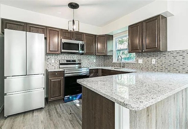 kitchen featuring appliances with stainless steel finishes, decorative light fixtures, dark brown cabinetry, and a peninsula