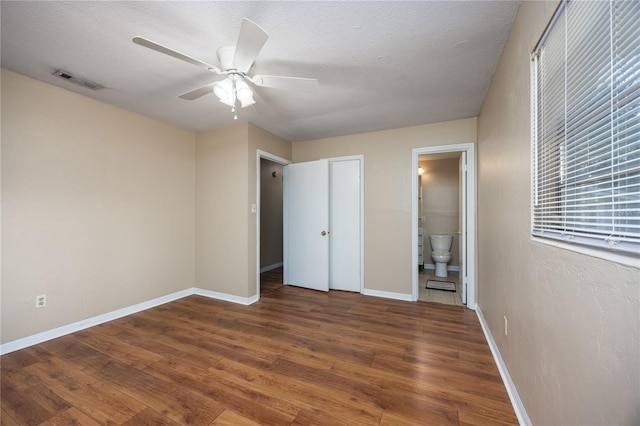 unfurnished bedroom with ceiling fan, dark wood-type flooring, a textured ceiling, and ensuite bath