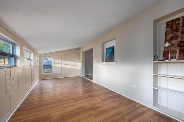 unfurnished room featuring lofted ceiling, hardwood / wood-style floors, and wooden walls