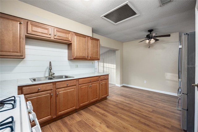 kitchen featuring sink, stainless steel fridge, wood-type flooring, a textured ceiling, and white gas range