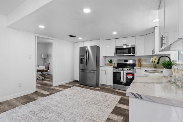 kitchen featuring appliances with stainless steel finishes, sink, white cabinets, dark hardwood / wood-style flooring, and light stone counters