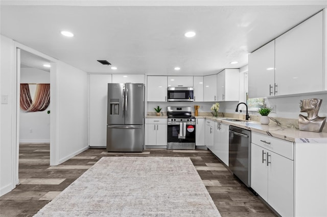 kitchen featuring appliances with stainless steel finishes, dark hardwood / wood-style floors, sink, white cabinets, and light stone countertops