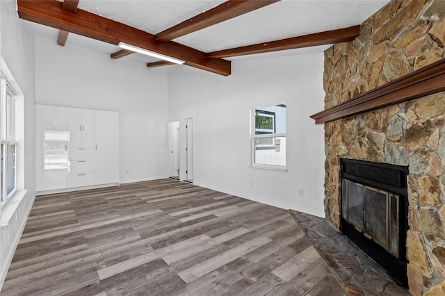 unfurnished living room featuring hardwood / wood-style flooring, a stone fireplace, and lofted ceiling with beams