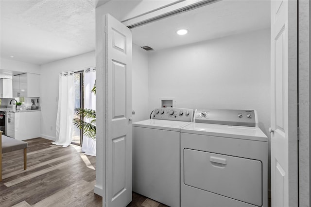 clothes washing area featuring sink, washing machine and dryer, and light wood-type flooring