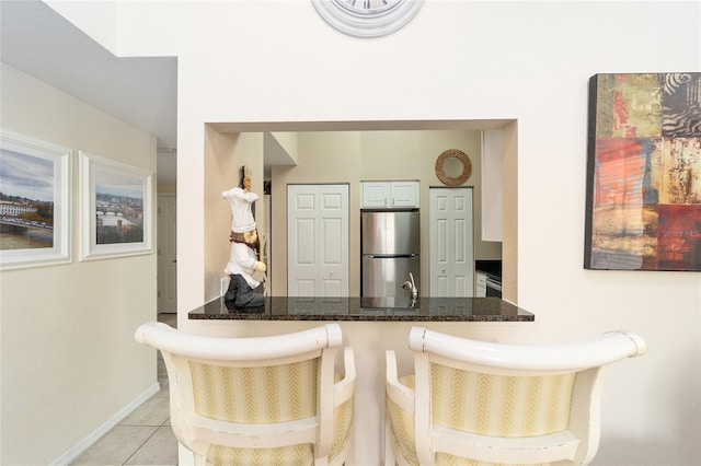 kitchen featuring stainless steel fridge, a breakfast bar, light tile patterned flooring, kitchen peninsula, and dark stone counters