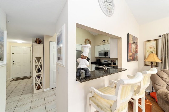 kitchen featuring light tile patterned floors, appliances with stainless steel finishes, kitchen peninsula, dark stone counters, and white cabinets