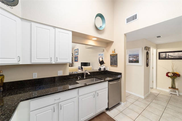 kitchen with sink, light tile patterned floors, stainless steel dishwasher, dark stone counters, and white cabinets