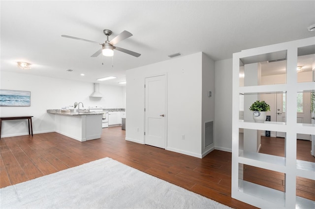 kitchen featuring wall chimney exhaust hood, white electric range, white cabinetry, dark hardwood / wood-style flooring, and kitchen peninsula